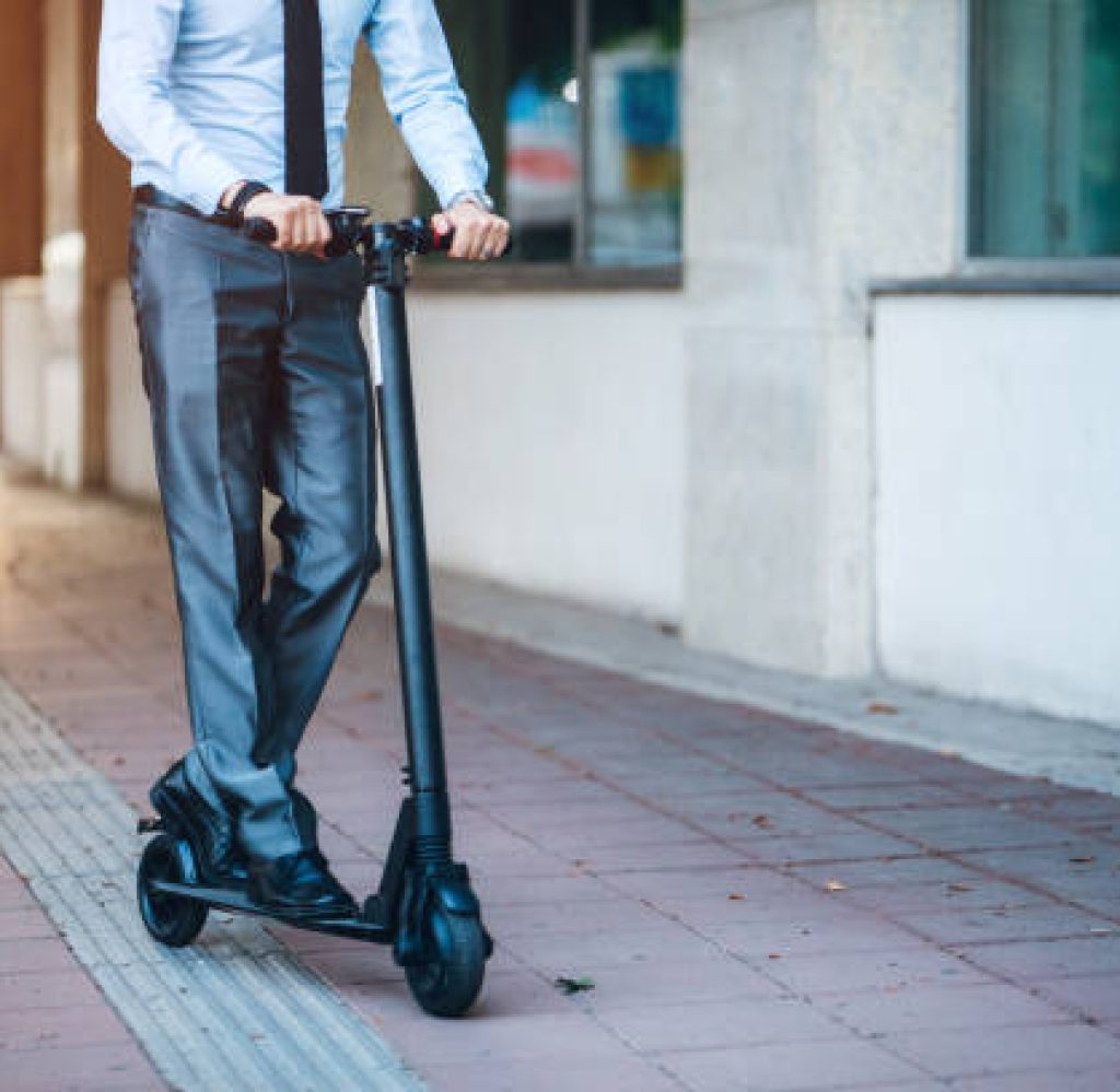 Young caucasian businessman  riding on electric push scooter through city in suit.