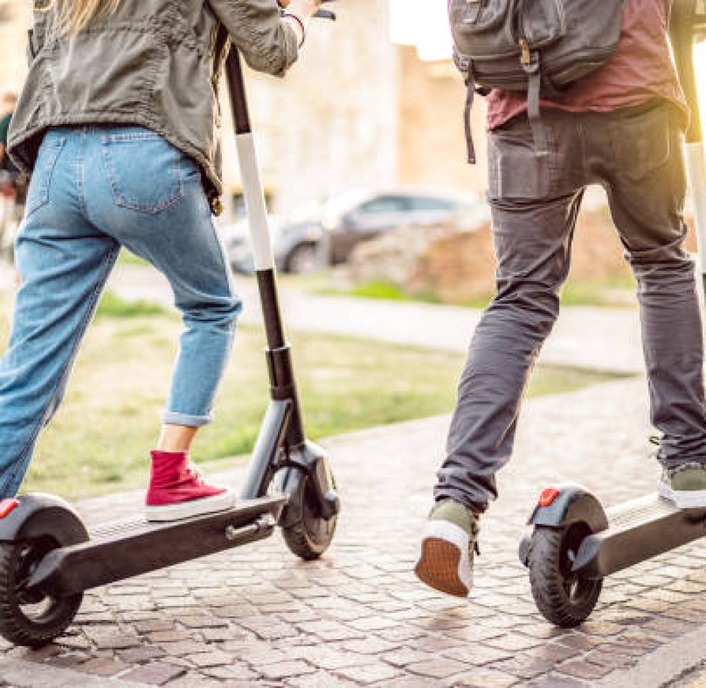 Millenial couple riding electric scooters at urban city park - Genz students using new ecological mean of transportation - Green eco energy concept with zero emission - Warm filter with sunshine halo